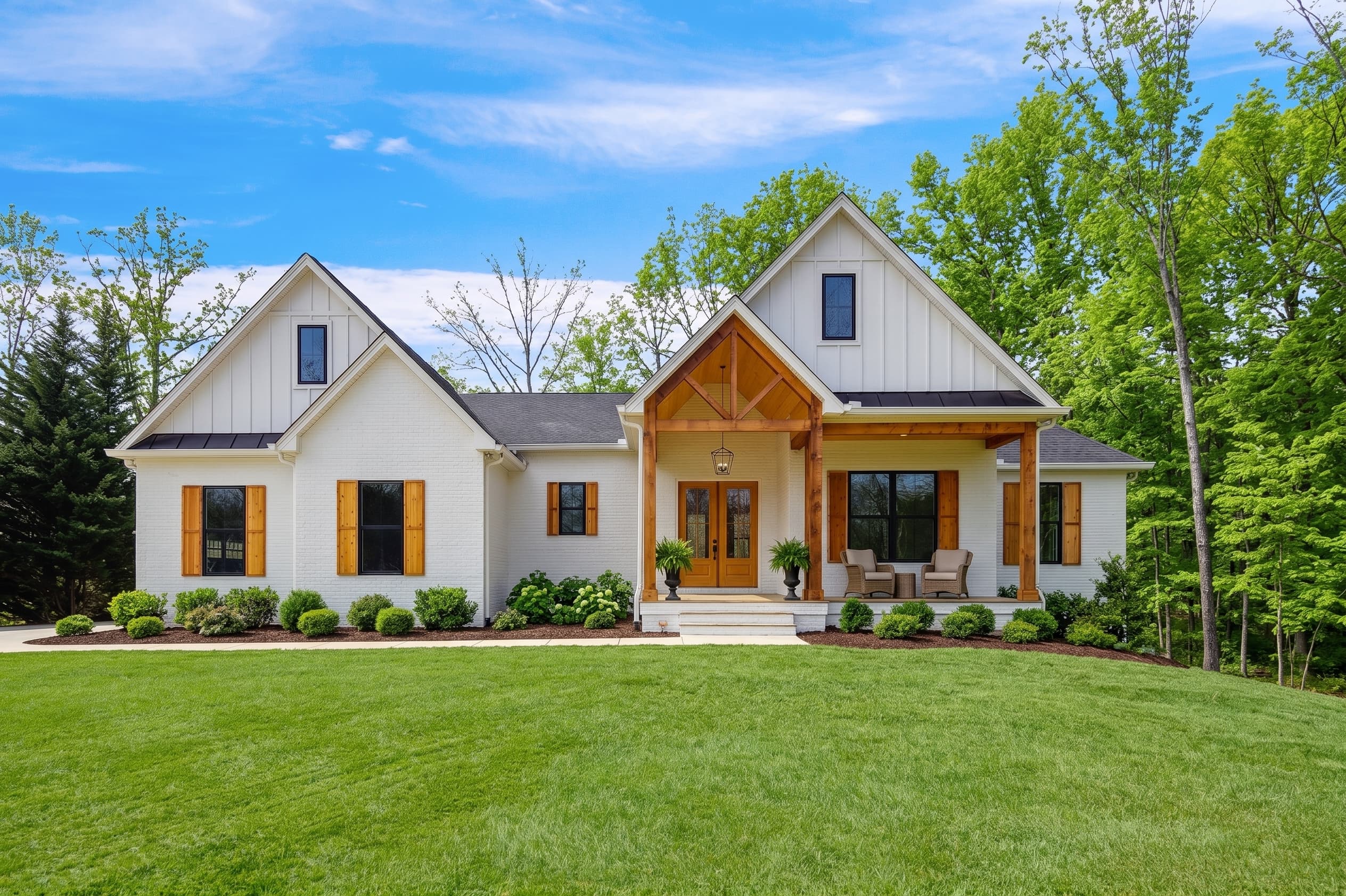 The Alexandria by Trigon Homes — a white brick and board-and-batten farmhouse with cedar timber porch posts, black metal roof accents and cedar shutters, on a landscaped lawn